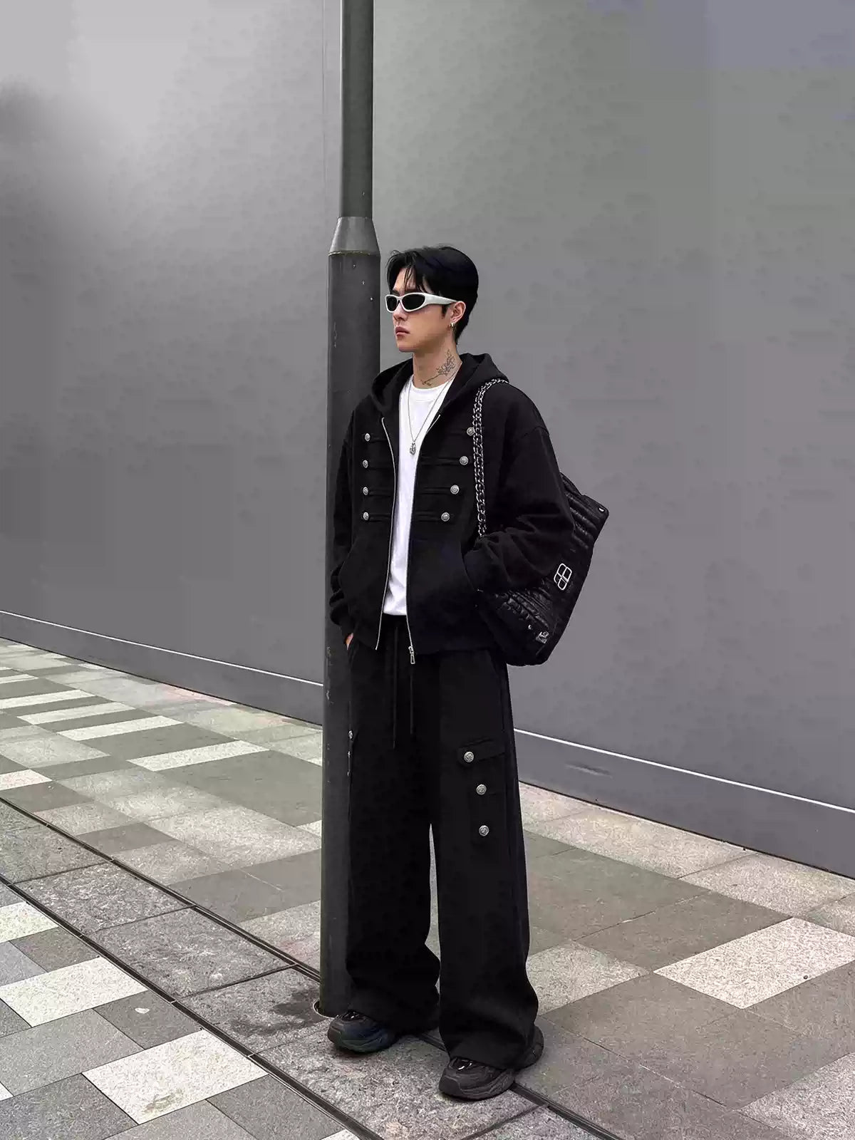 メンズの黒のセットアップを斜め横から写した全身。パンツの脇ポケットのフラップに銀ボタンが3つ並ぶ、ゆったりした形。