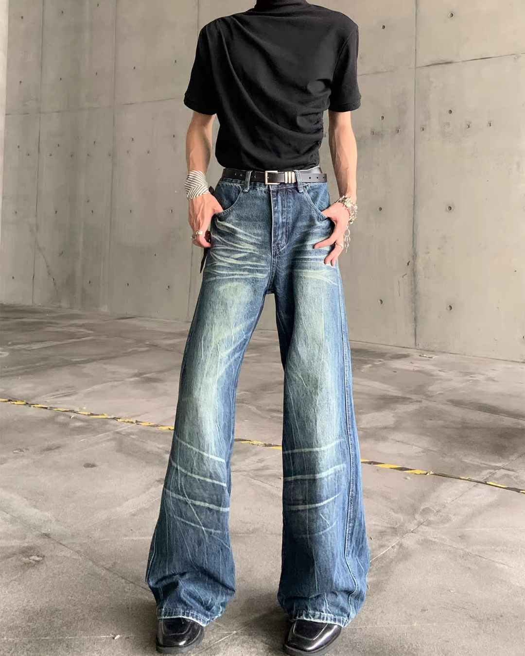 メンズの濃いインディゴのデニムパンツ。右腕を下げ、膝下に白い横ジワ加工、裾へ向かって太く広がる。黒カットソーを合わせる