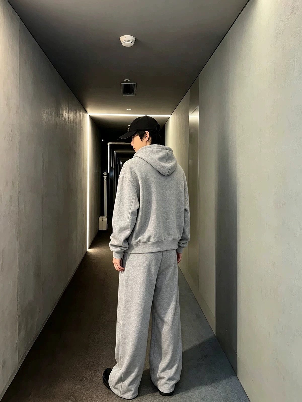 メンズのグレーのセットアップの背面。無地のフード付きパーカーとワイドパンツを、後ろから写した全身の着用写真。