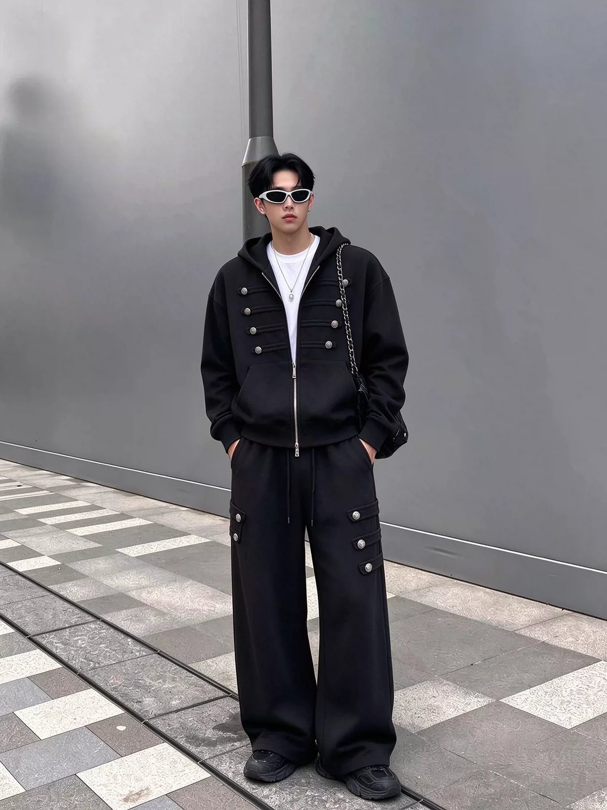 メンズの黒のセットアップを正面から写した全身。胸に4段のボタン飾りが付いた短め丈のパーカーと、裾まで広がるワイドパンツ。
