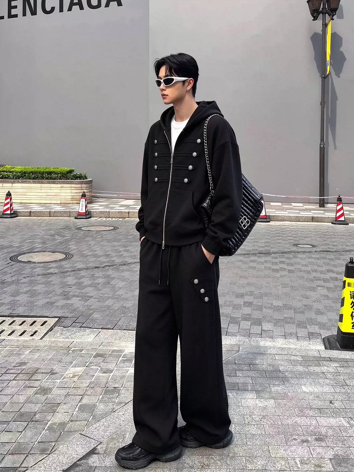 メンズの黒のパーカーとワイドスウェットパンツのセットアップ。パンツの脇にも銀ボタンが付く、横向きの全身の着用写真。