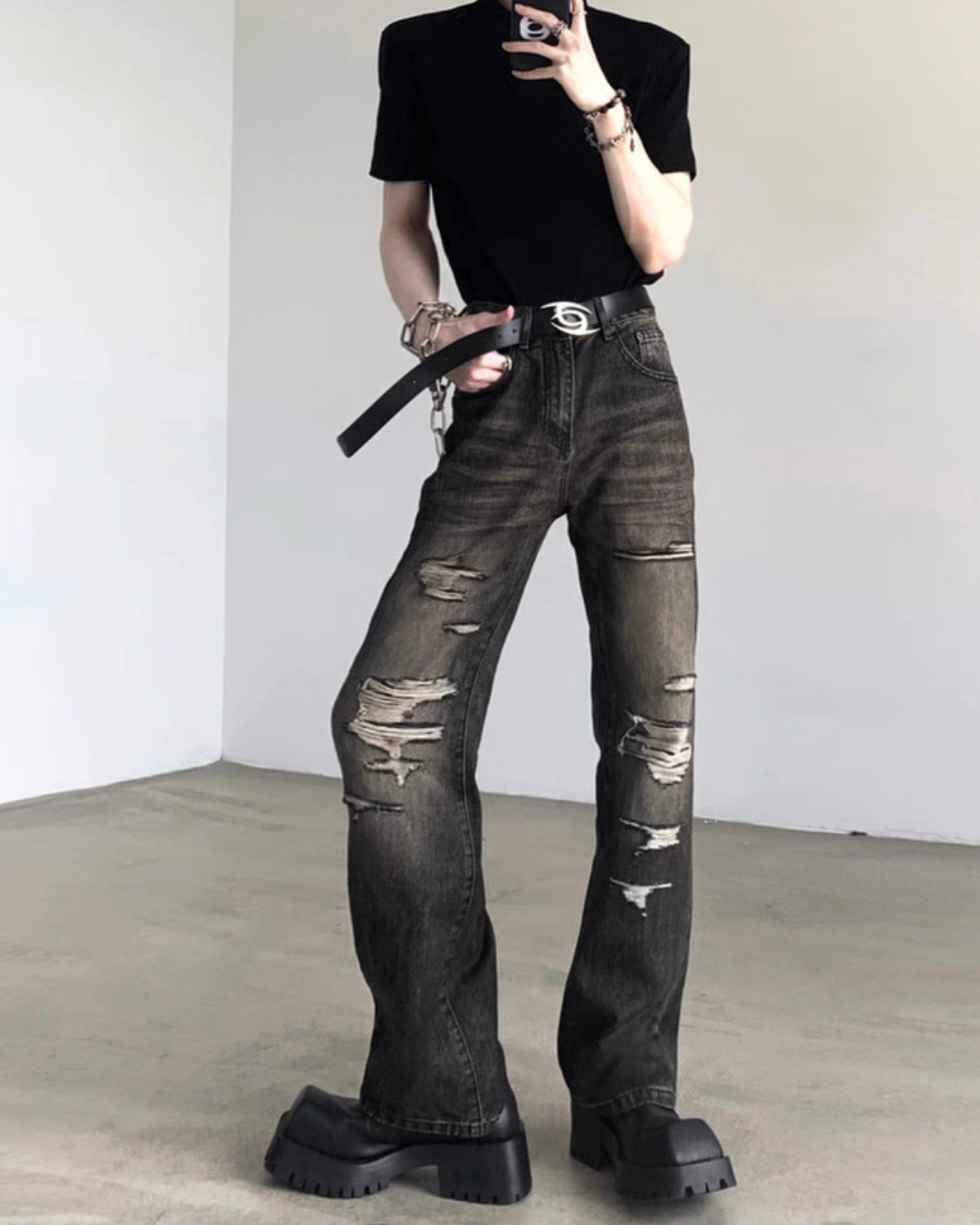 黒半袖Tシャツと黒ダメージデニムパンツの着用画像。デニムは膝から大腿部にかけて大きく破れた加工で、ウエストに黒レザーベルト装着。厚底ブーツ合わせ。