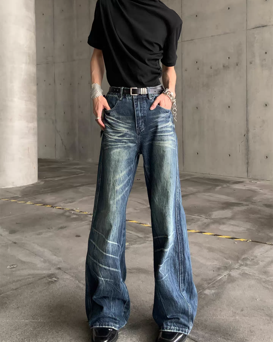 メンズの青みのウォッシュ加工とひげ落ちが入ったフレアデニムパンツ。黒ベルトを通すハイウエストで、裾に向かって広がる正面の着用写真。
