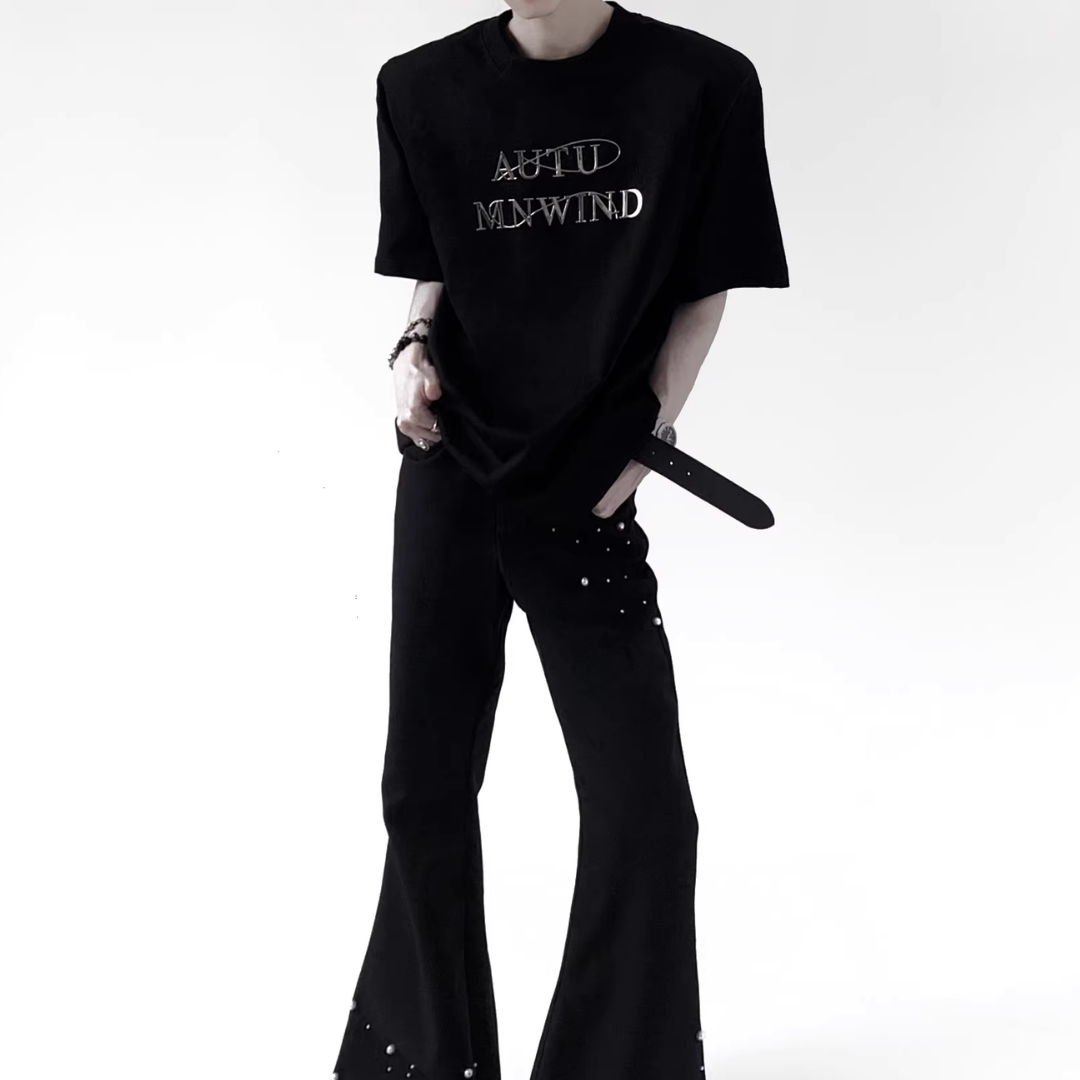 黒のオーバーサイズTシャツ。胸部にメタリック銀色のロゴプリント。半袖でクルーネック。