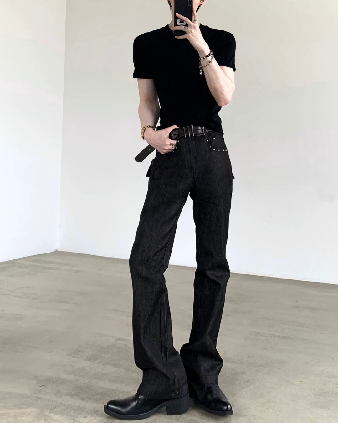 メンズの黒半袖カットソーと黒デニムパンツ。パンツはハイウエスト、裾にスリット入り。黒レザーベルトで装飾。