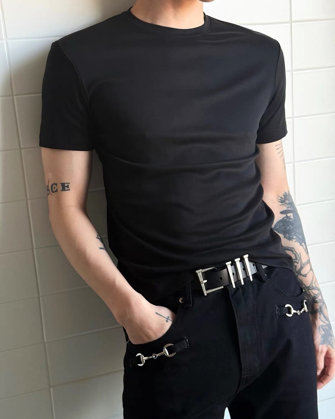 黒半袖クルーネックカットソー。シンプルなスリムフィットで、ショート丈。暗紺デニムパンツとメタルバックル付きベルトの着用例。