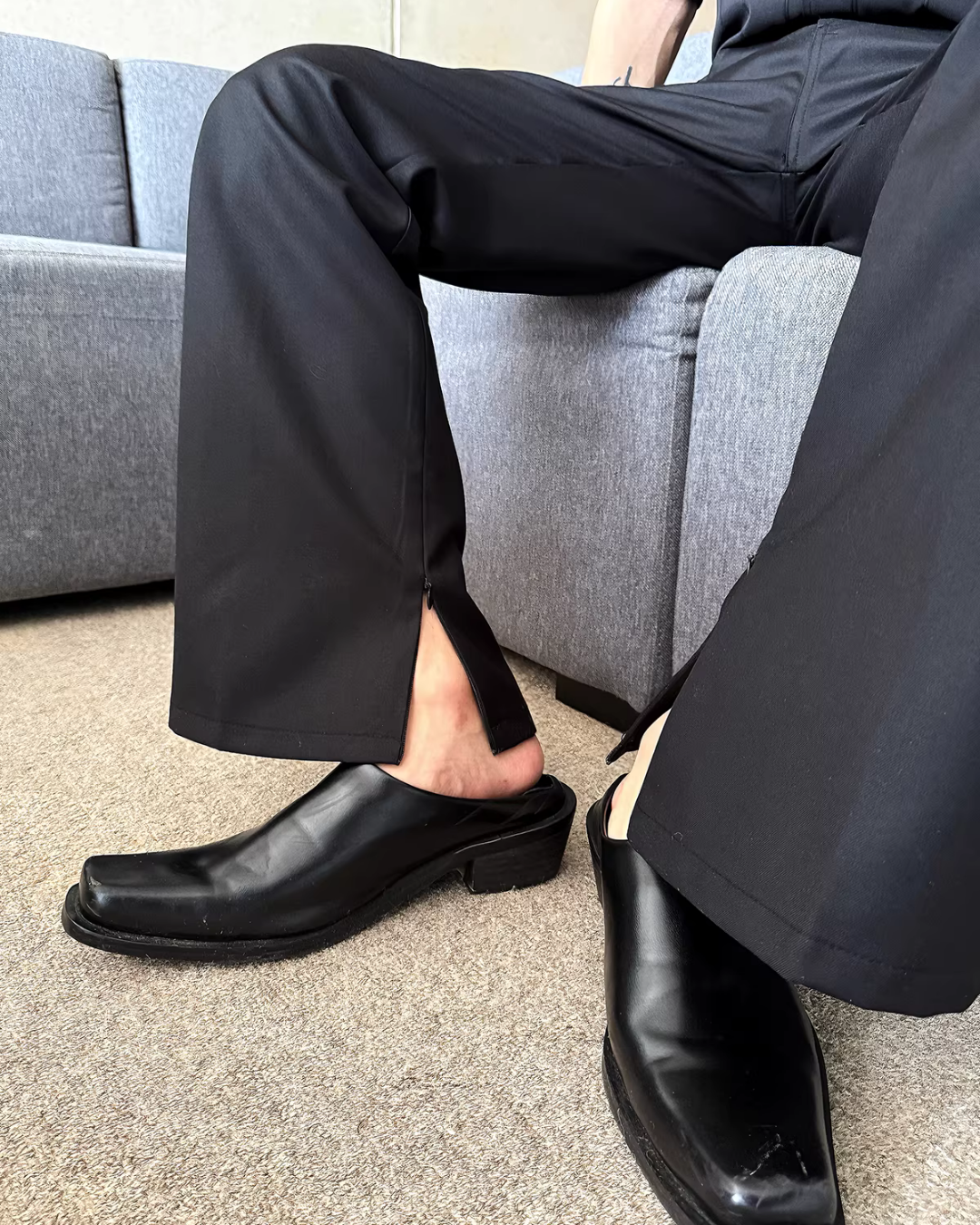 メンズの黒のストレートレッグパンツ。裾にスリット入り、素材はツイル地。モデル着用、座位でのローアングル全身撮影。
