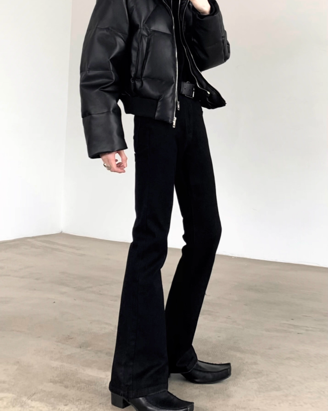 メンズの黒デニムのハイウエストフレアパンツ。腰から裾にかけて広がるシルエットで、長丈に仕上げた全身着用画像。