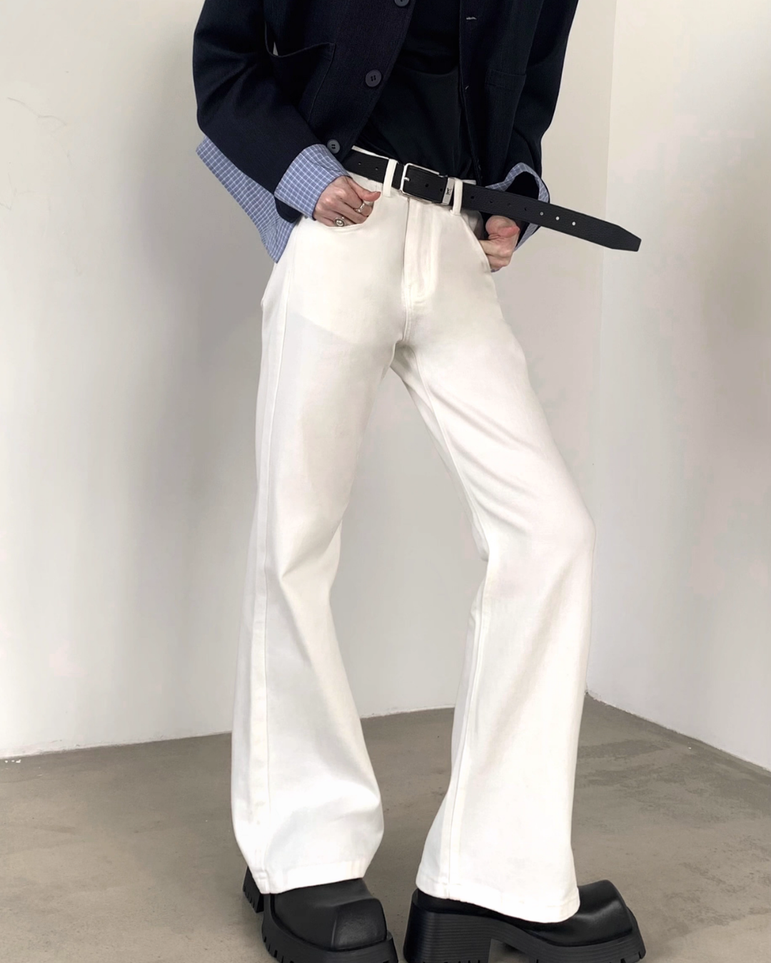 メンズの白のハイウエストフレアデニムパンツ。黒のベルト付きで、裾に向かって広がるシルエット。