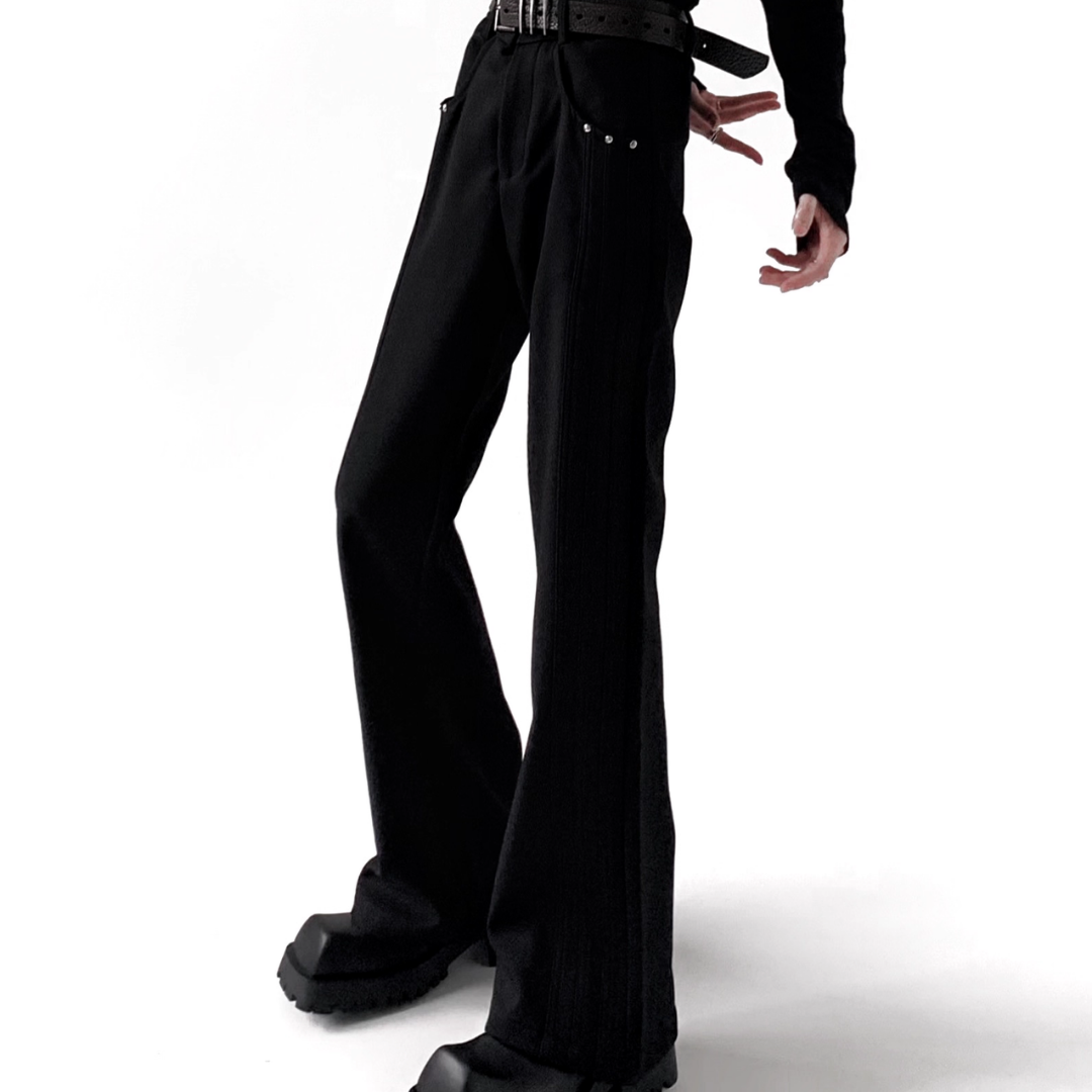 黒のフレアパンツ。ハイウエストで幅広いベルト付き、スタッズ装飾とスリット入り。裾に向かって広がるシルエット。