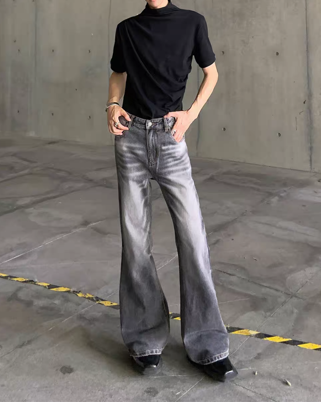 メンズのグレーのウォッシュデニムのフレアパンツ。両手をポケットに入れた着用写真で、前立てのボタンと裾の広がりが見える。