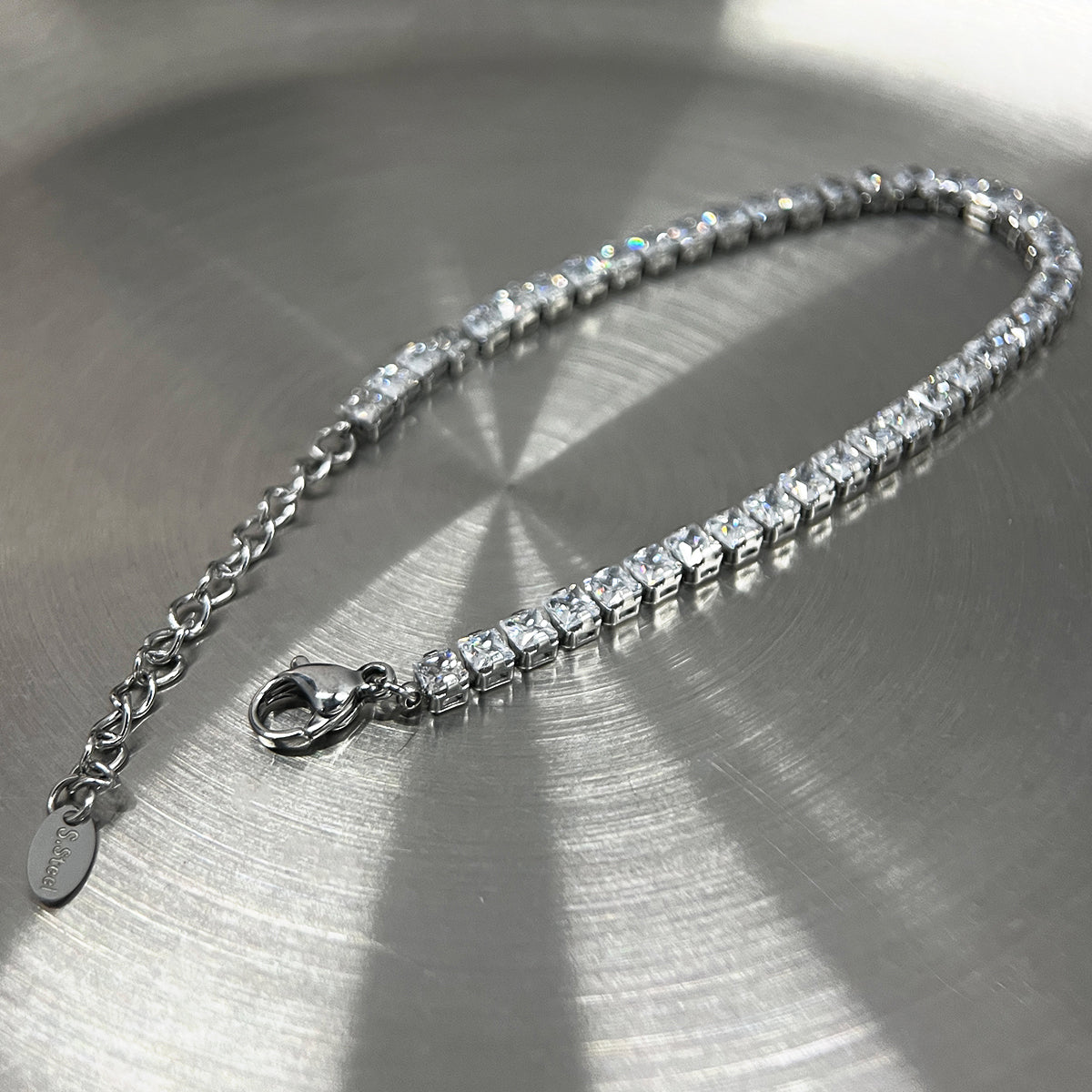 メンズのシルバートーンの金属チェーンにクリスタルストーンを連ねたテニスブレスレット。ロブスタークラスプと小型プレート付き。