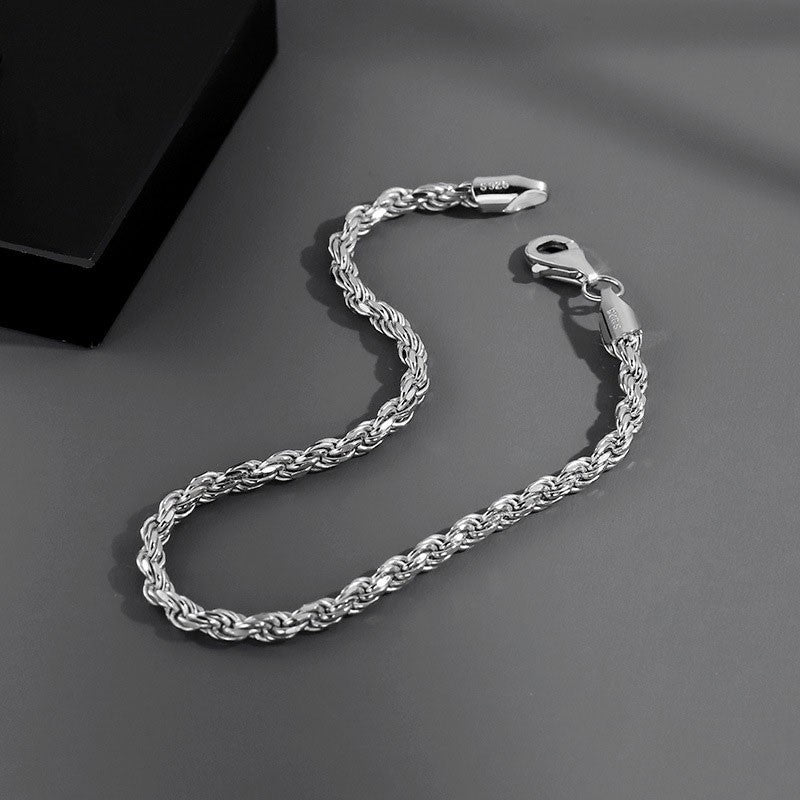 メンズのねじり編みのシルバーのチェーンブレスレットを斜めに置いた画像。留め具の金具に刻印が見える。