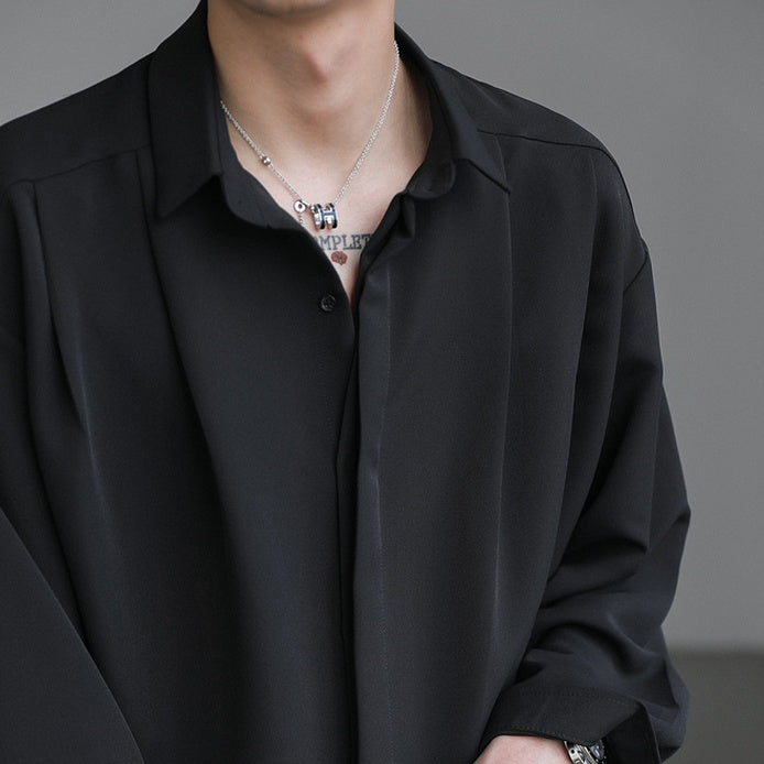 メンズの黒いコットン素材のシャツ。開襟で前身頃にタック入り、ゆったりしたシルエット。長袖。