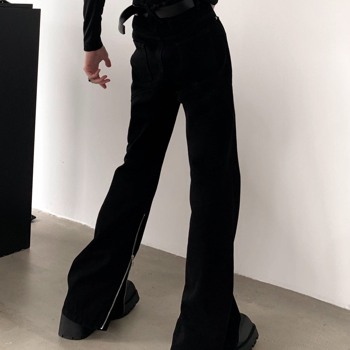 黒のフレアパンツの後ろ姿。ヒップのポケットと脇のすそ付近のファスナー、広がるすそ口が見える。
