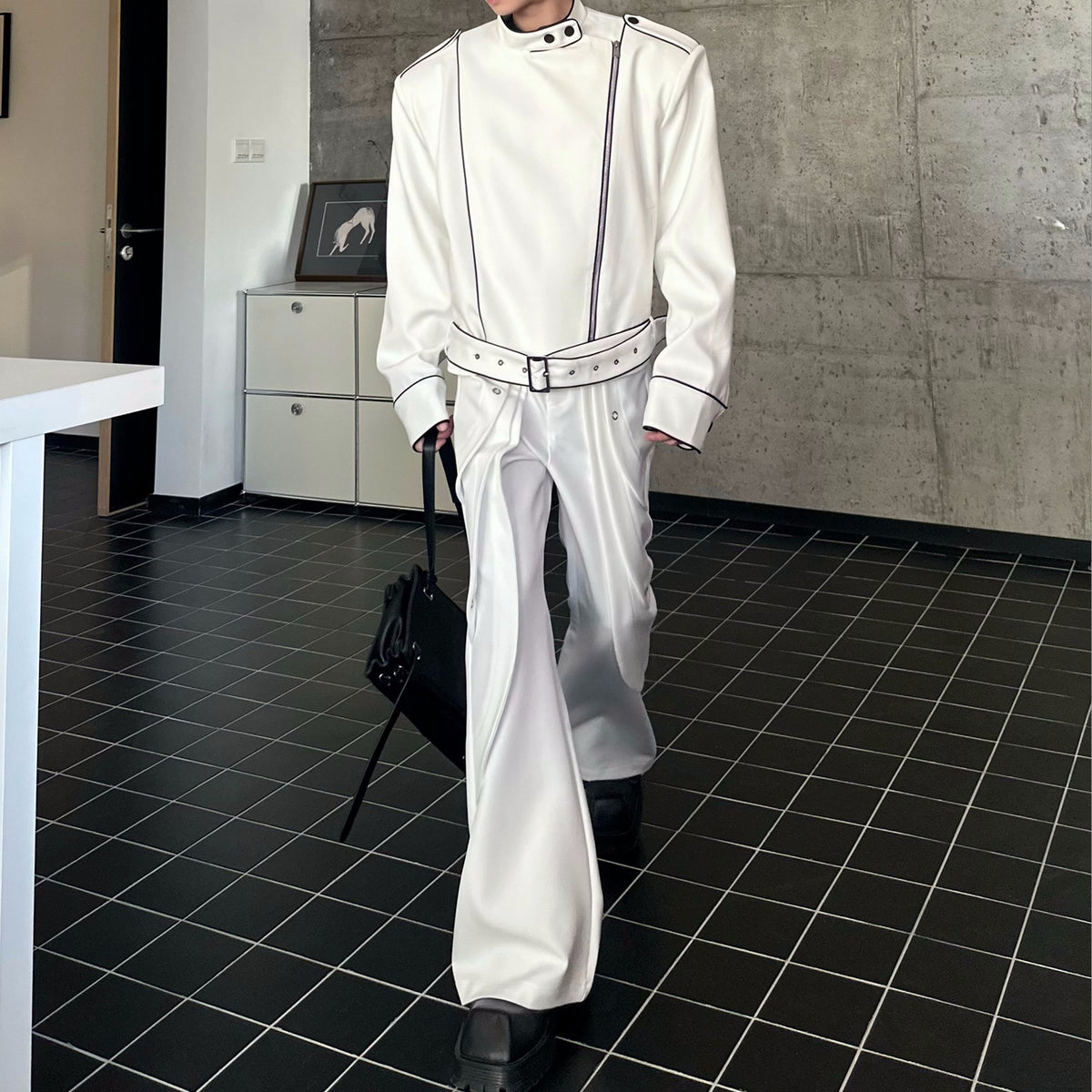 メンズの白のフレアパンツの全身。側面にドレープ状の重なりが入り、黒パイピングの白いジップトップスとベルトを合わせた。