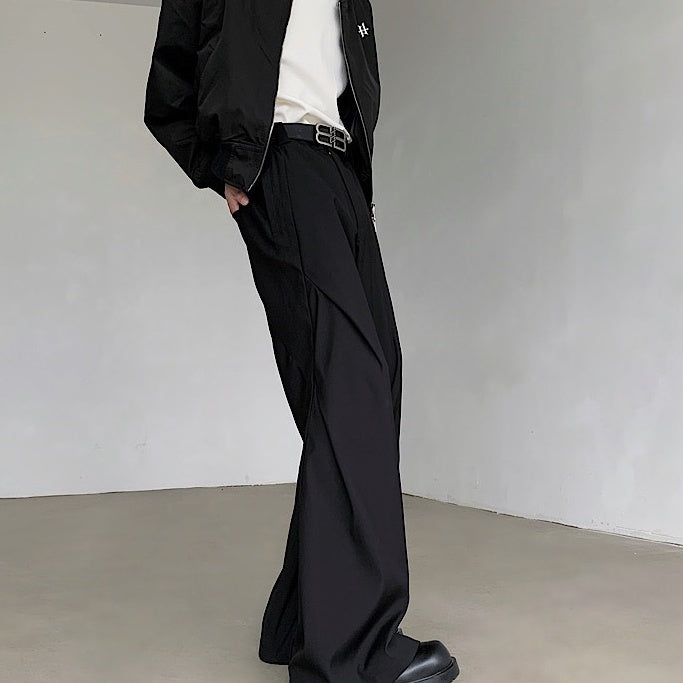 黒いドレープパンツ。ウエスト二重ベルト付き、くるぶし丈、ワイドシルエット。素材に光沢感があり、腰から裾にかけてドレープが流れる。