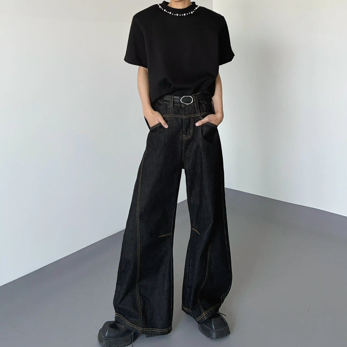 黒デニムのハイウエストワイドパンツ。ステッチディテールとリング金具ベルト付き。裾は広がったシルエット。