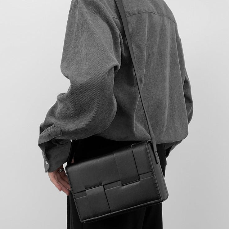 黒レザーのショルダーバッグ。パッチワーク風のクロス切替ディテール、フラップ式開口部、調整可能なストラップ付き。