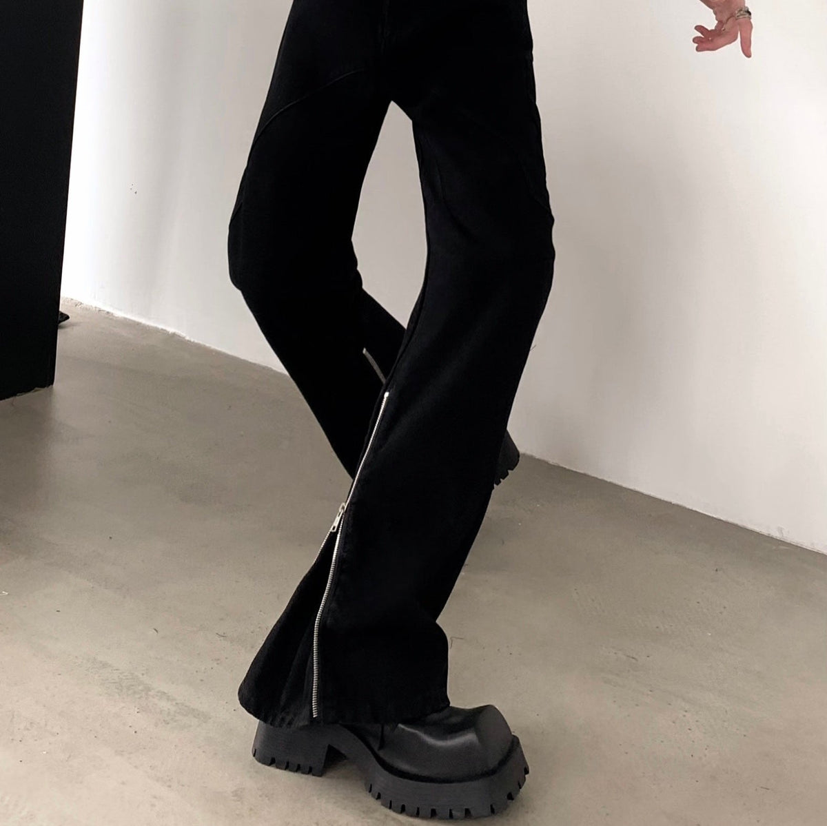 黒のフレアパンツを斜め前から写した着用。脚の外側に細いファスナーがすそまで通り、厚底ブーツを合わせる。