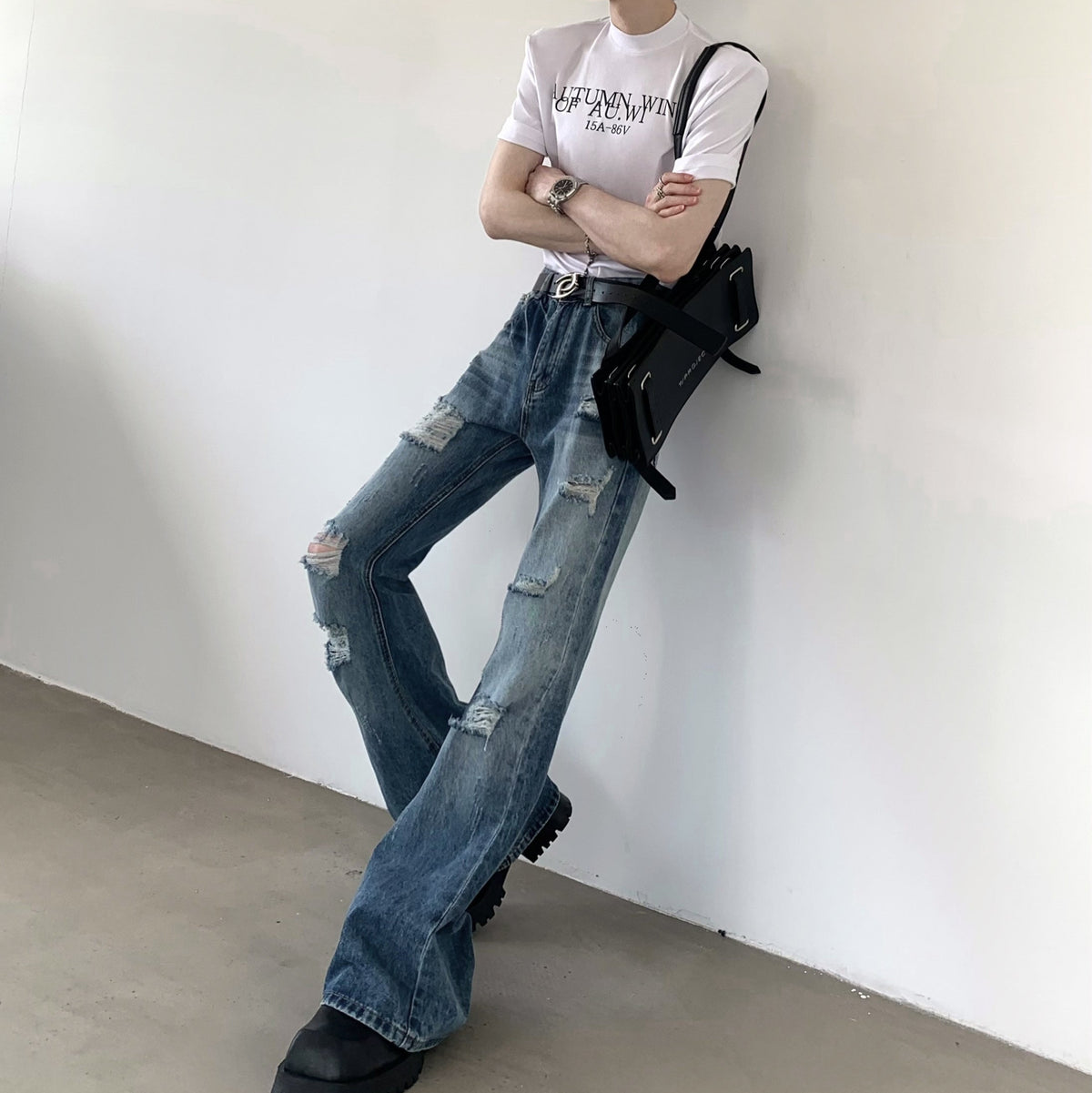 白地にロゴプリントされたクルーネック半袖Tシャツ。ストレッチデニムのダメージ加工ワイドパンツとスタイリングされた着用画像。