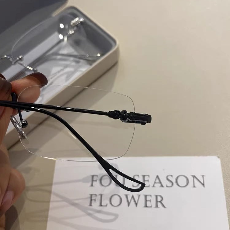 メンズの手に持った黒フレームのリムレスメガネのテンプル寄り。結び目状の装飾の入った先端と、穴のあいた耳掛け部、縁なしレンズ。