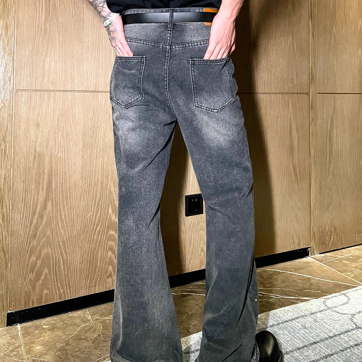 メンズのグレー系に洗い加工したデニムパンツ。後ろポケットに黒いワッペン付き、裾に向けてフレアシルエット。