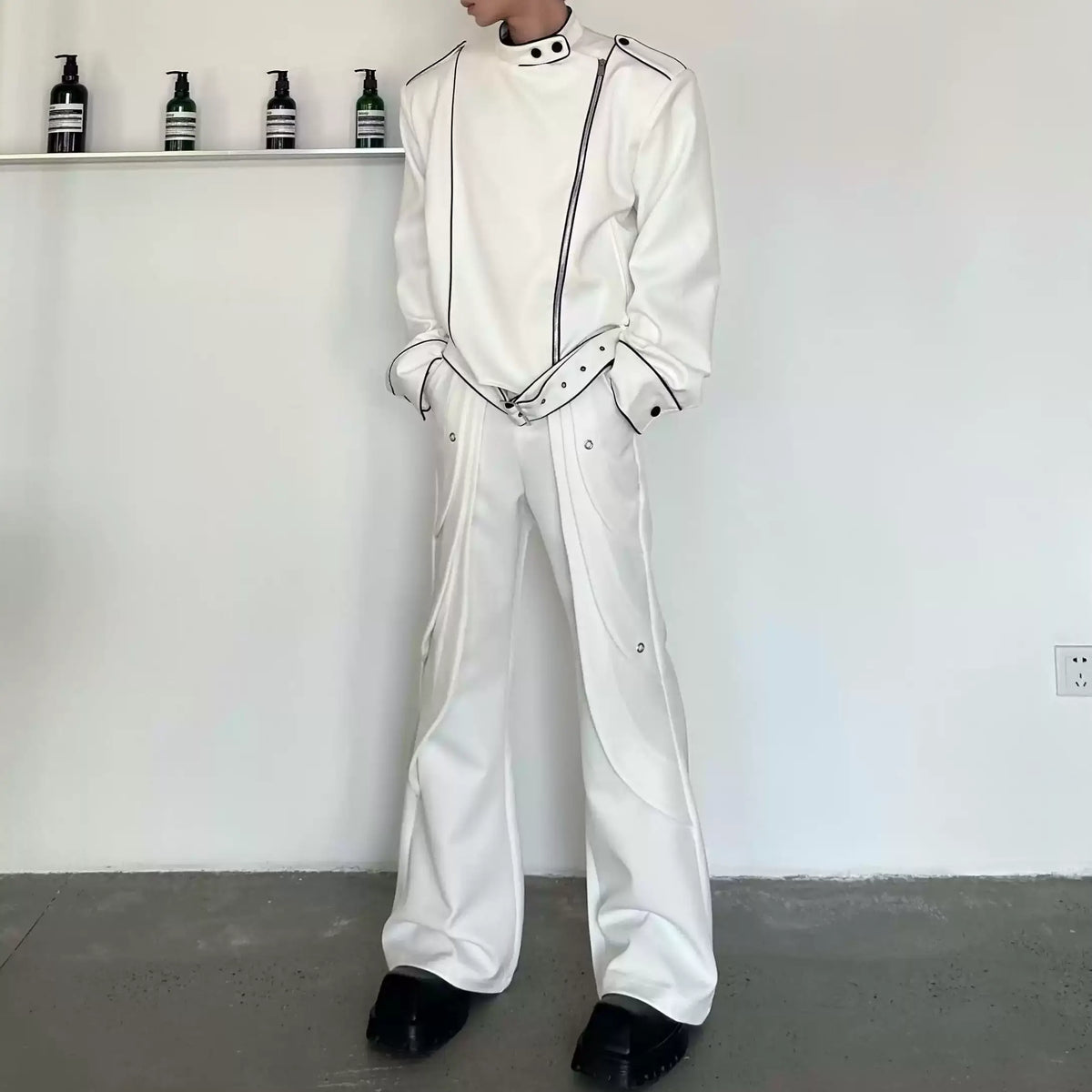 メンズの白のフレアパンツ。側面にハトメ金具と曲線のレイヤー切り替えが入り、黒パイピングの白ジャケットを合わせた全身。