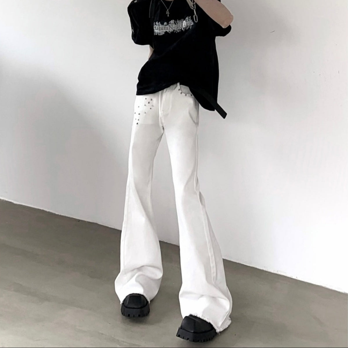 メンズの白デニムのフレアパンツ。ハイウエスト、腰部分にスタッズ装飾、センターにドレープ。裾はフレアで広がり、厚底ブーツとの着用例。