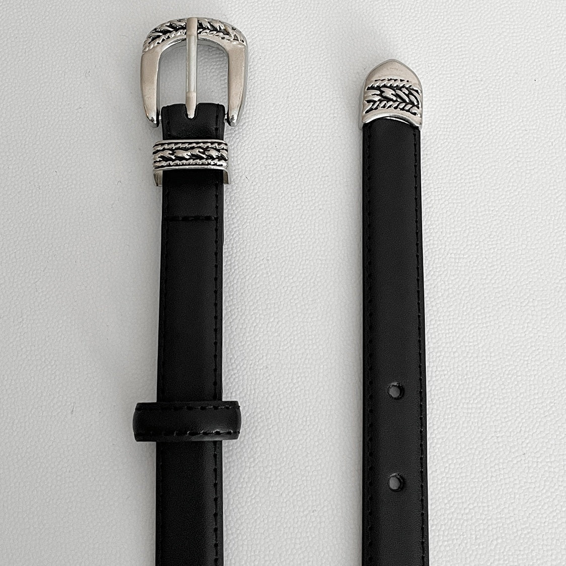 メンズのベルトのバックル側と先端側を縦に並べた寄り画像。黒レザーにステッチ入りで、柄入りシルバー金具が付く。