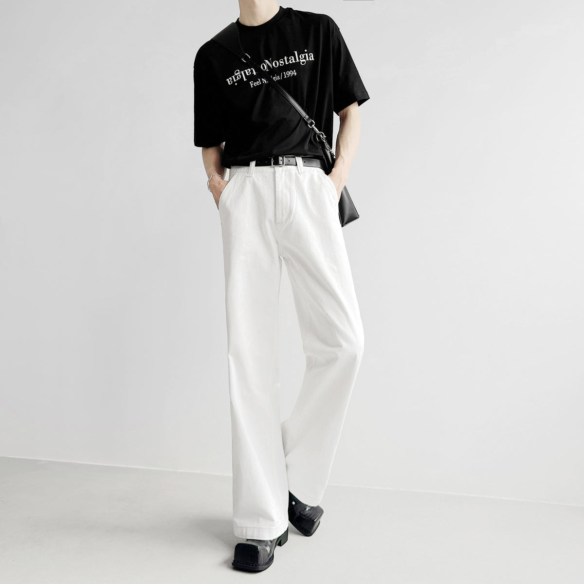 白のルーズフィットデニムパンツ。ハイウエスト、タック入りで、アンクル丈。黒いカットソーとベルト合わせのスタイリング。