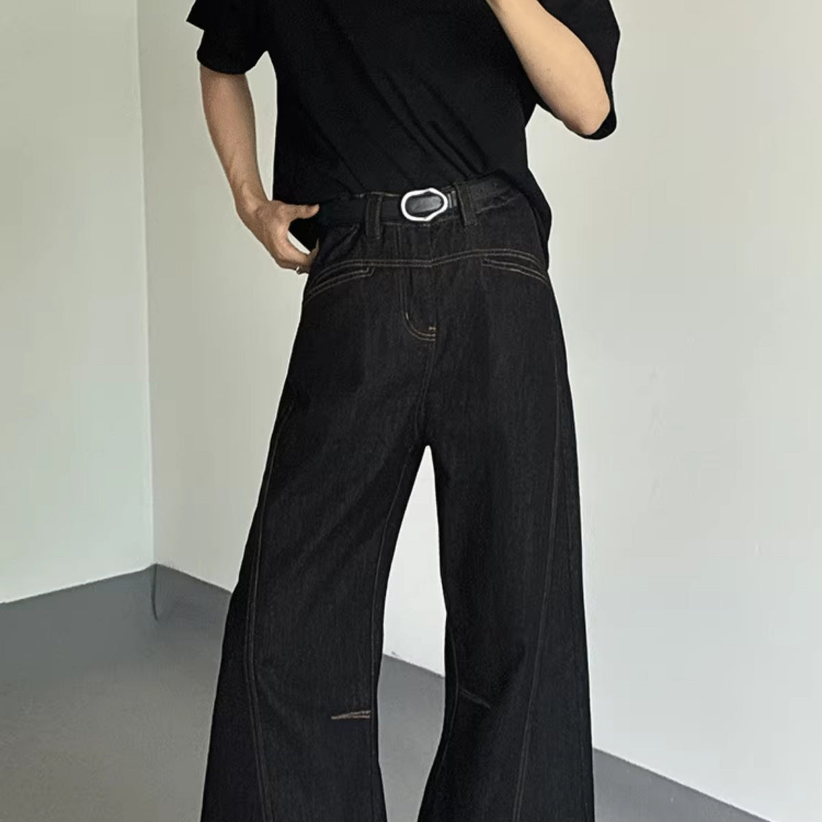 メンズの黒デニムのハイウエストパンツ。ステッチディテールとメタル付きベルト、膝部分にスリット入り。ワイドシルエット。