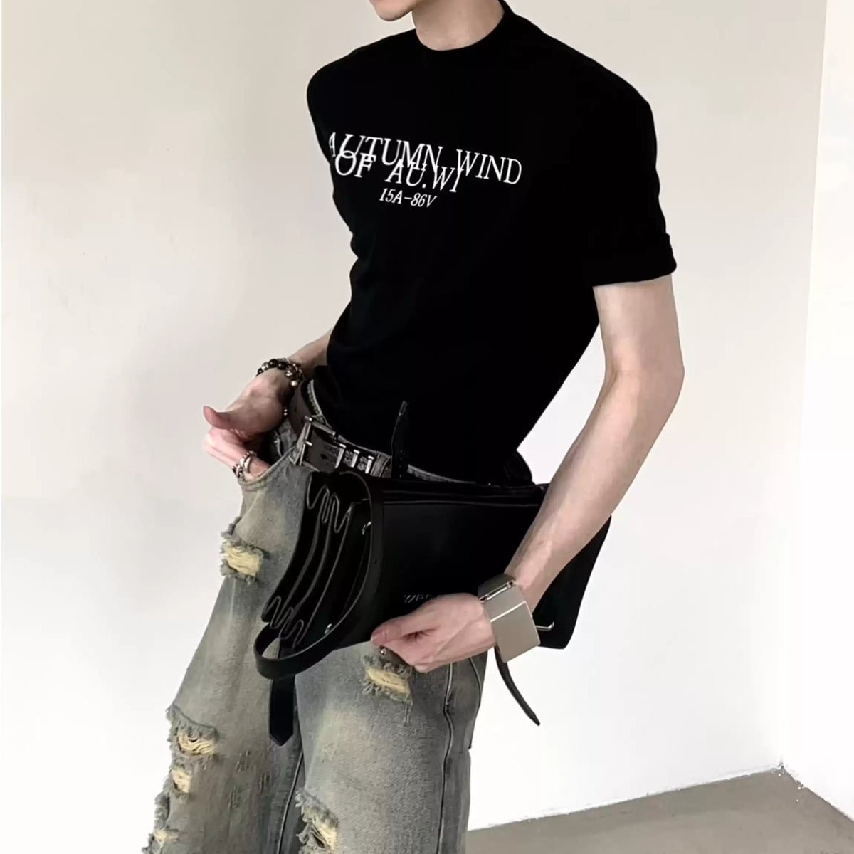 黒の半袖カットソー。胸部に白いテキストロゴプリント。グレーのダメージデニムパンツと黒のショルダーバッグを合わせたスタイリング。