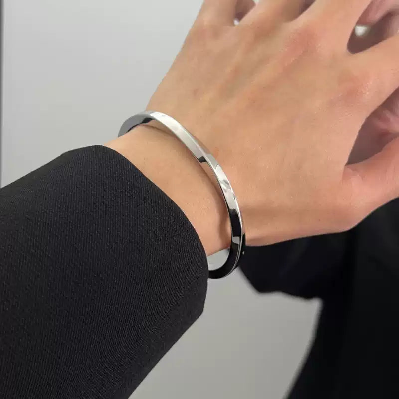メンズの手首に着けた銀色のねじりバングル。光沢のある細身のオープンタイプで、黒の袖と手の甲の間に収まった着用写真。