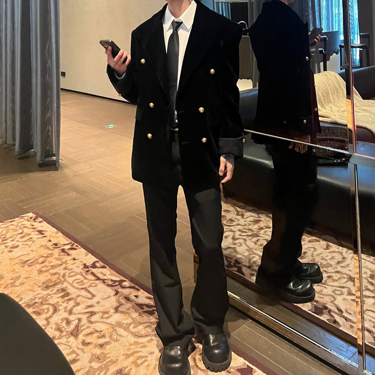 メンズの黒のダブルブレストジャケットの全身着用。携帯を持ち、黒のフレアパンツとボリュームソールの黒い靴を合わせている。鏡の前で撮影。