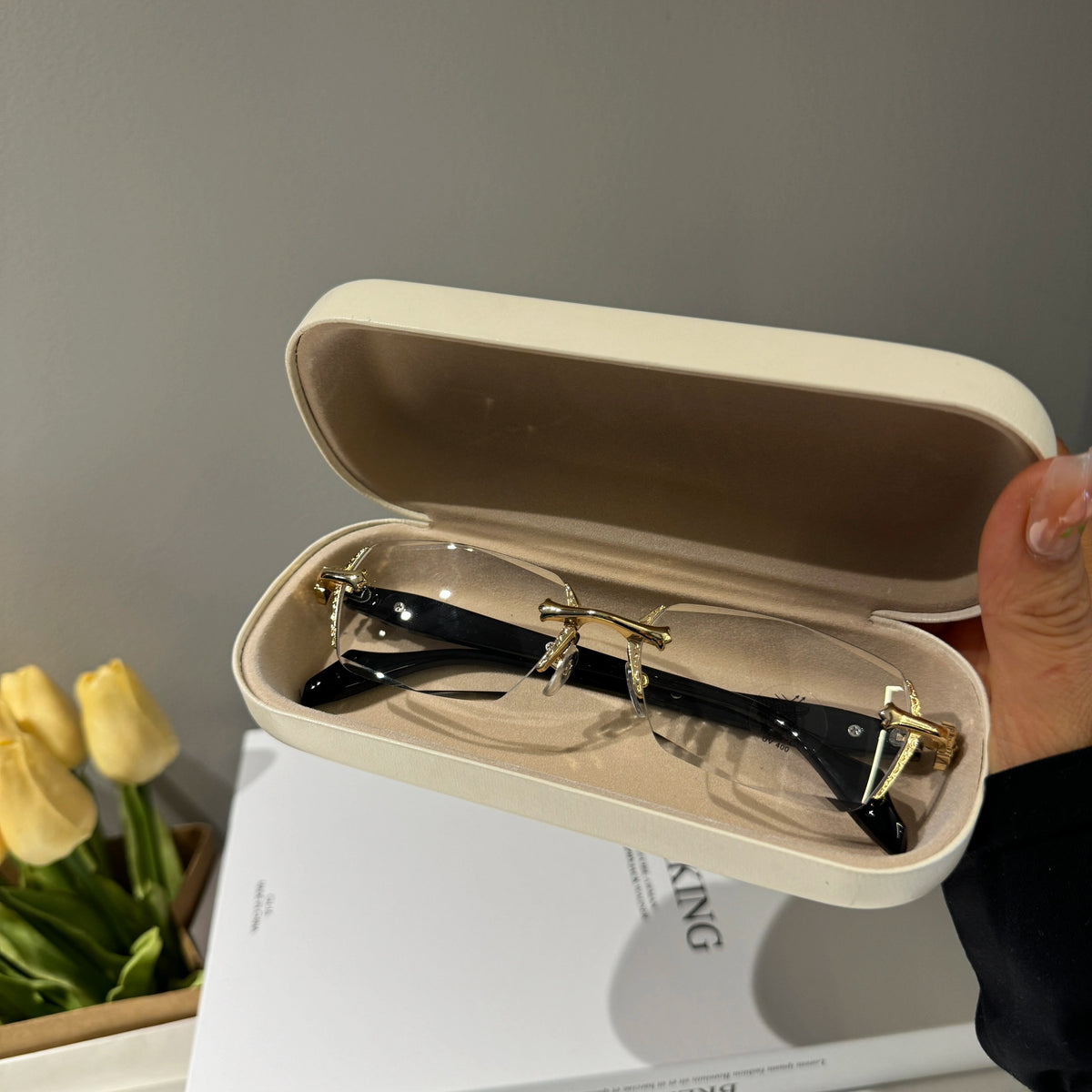 メンズの開いたベージュのケースに、金色の金具のリムレス眼鏡を収めた画像。黒いテンプルと無色のレンズが写る。