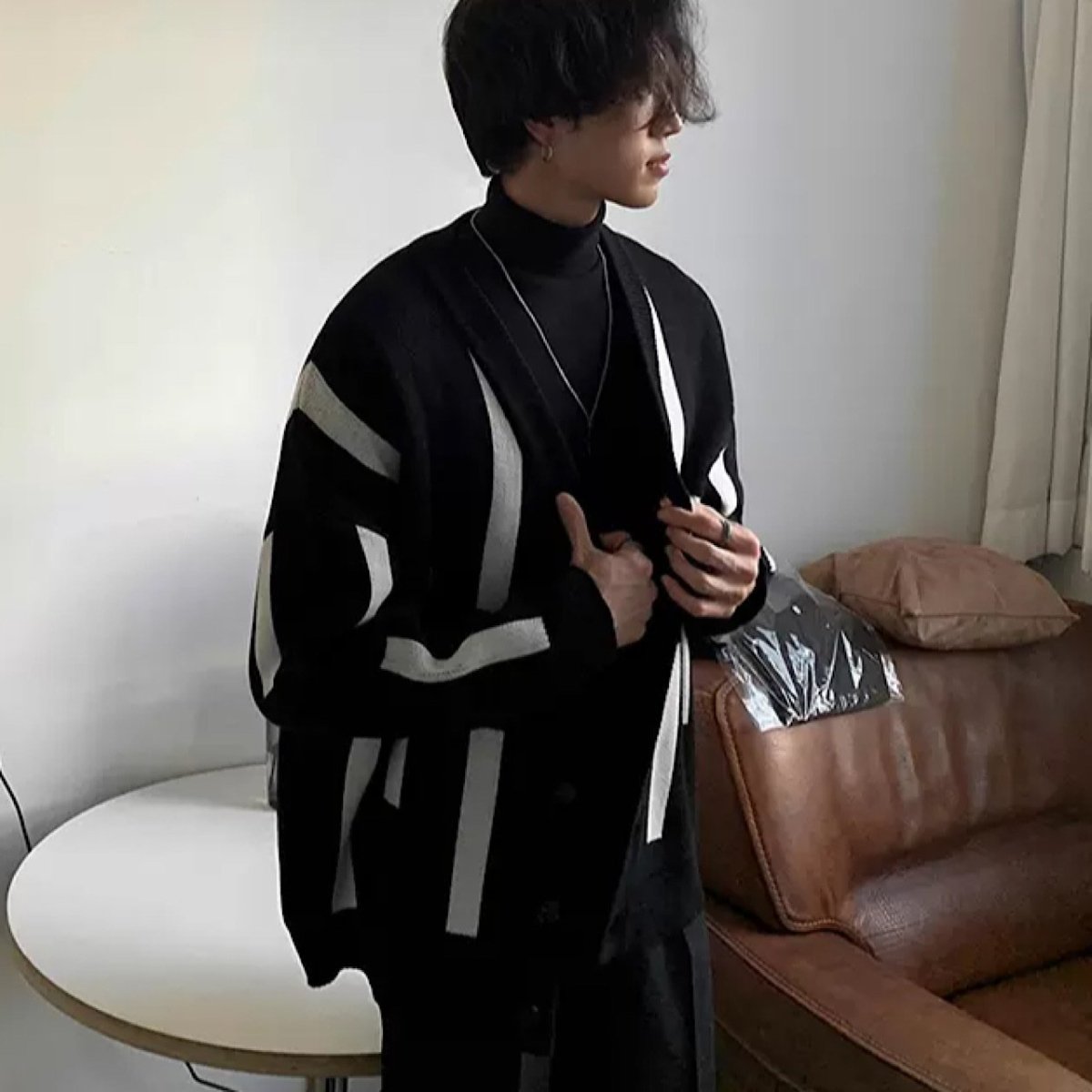 黒地に白とグレーの幾何学模様が入ったロングカーディガン。オーバーサイズシルエットで前開き、黒のタートルネックニットと合わせた着用画像。