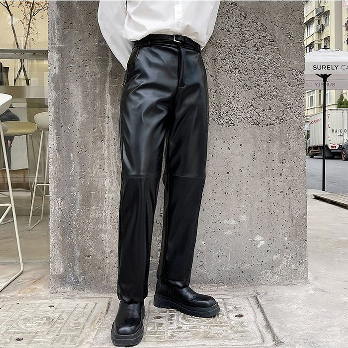 黒いレザースラックス。光沢のある素材でストレートなシルエット。ウエスト部分にセンタープレスが入り、足首まで長い着丈。ブーツと合わせたモード系スタイリング。