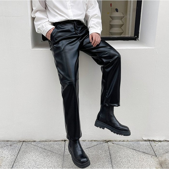 黒のエナメルレザースラックス。ウエストゴム仕様で、ドレープを持つストレートシルエット。裾は広がりのあるレングス。
