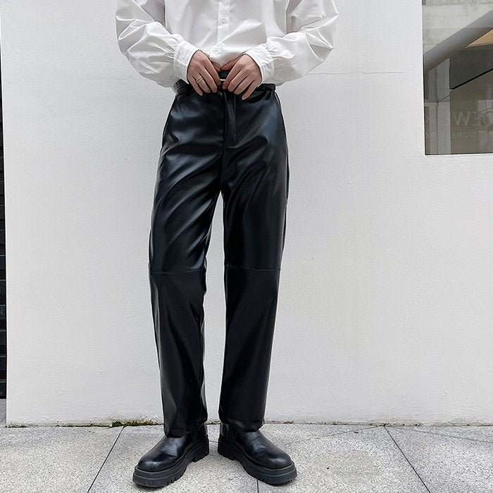 黒いレザーパンツ。光沢のある素材で、ウエストから裾に向けてタック状のドレープが入り、直線的なシルエット。ハイウエスト設定。