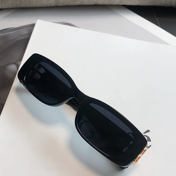 メンズの黒いプラスチックフレームのサングラス。矩形レンズに濃色のティンテッドレンズ。テンプル部分にゴールド金具装飾。