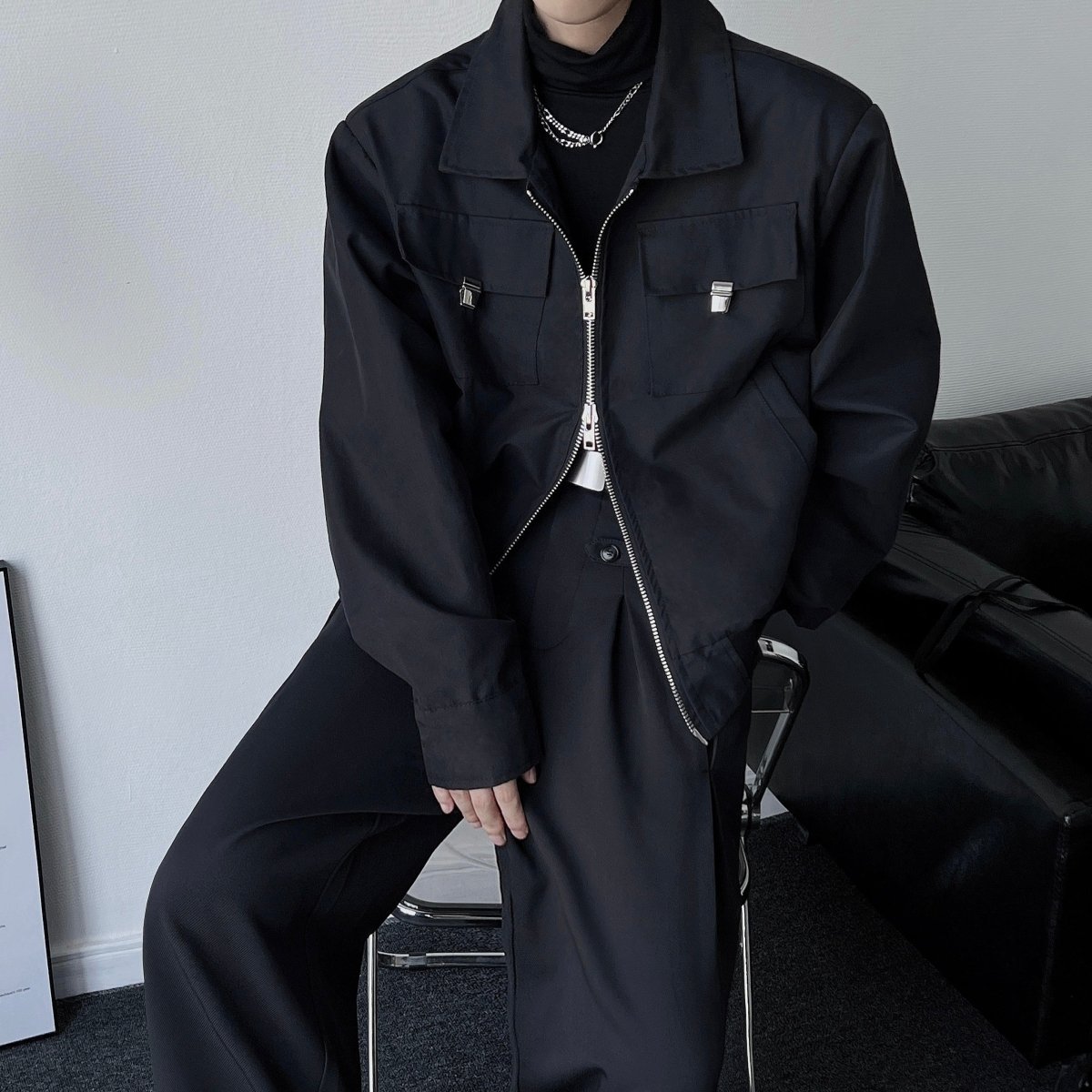 黒のロングジップジャケット。オーバーサイズシルエット、広い襟、前面にフラップポケット2つ、銀色の大型ジップ、コットン混素材。