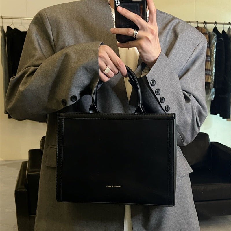 黒レザーのスクエア型ハンドバッグ。シンプルな上部ハンドルと立体的なボックスシルエット、ブランドロゴ入り。