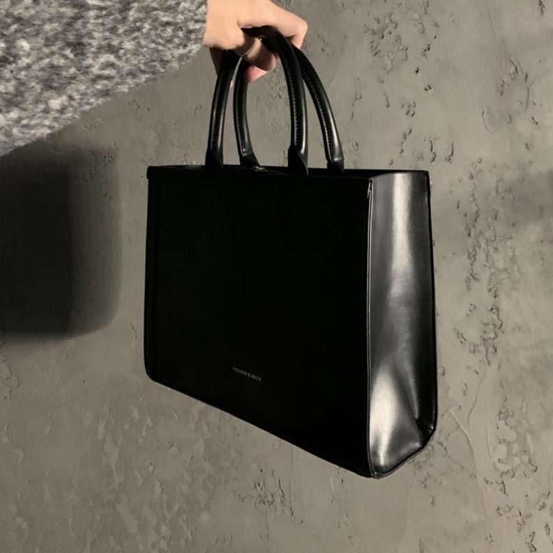 黒レザーのトートハンドバッグ。マット素材と光沢のある側面のコントラストが特徴。太めの2本ハンドル付き。
