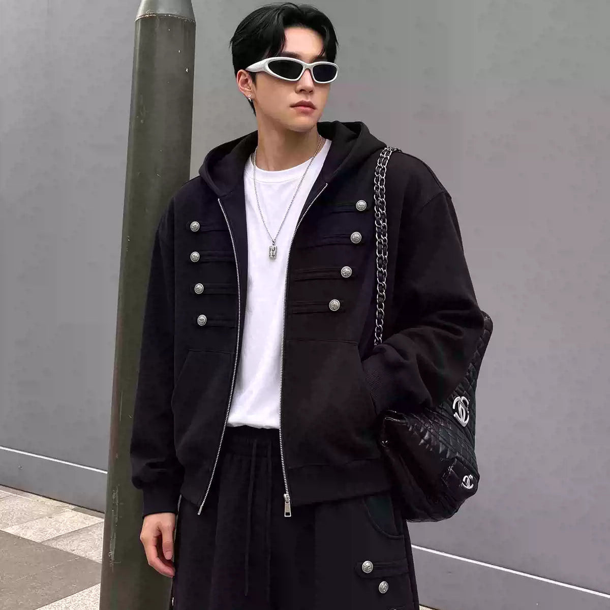 メンズの黒のスウェットジップパーカー。胸に銀ボタンとライン飾りが4段並び、白Tシャツの上に羽織った上半身の着用写真。