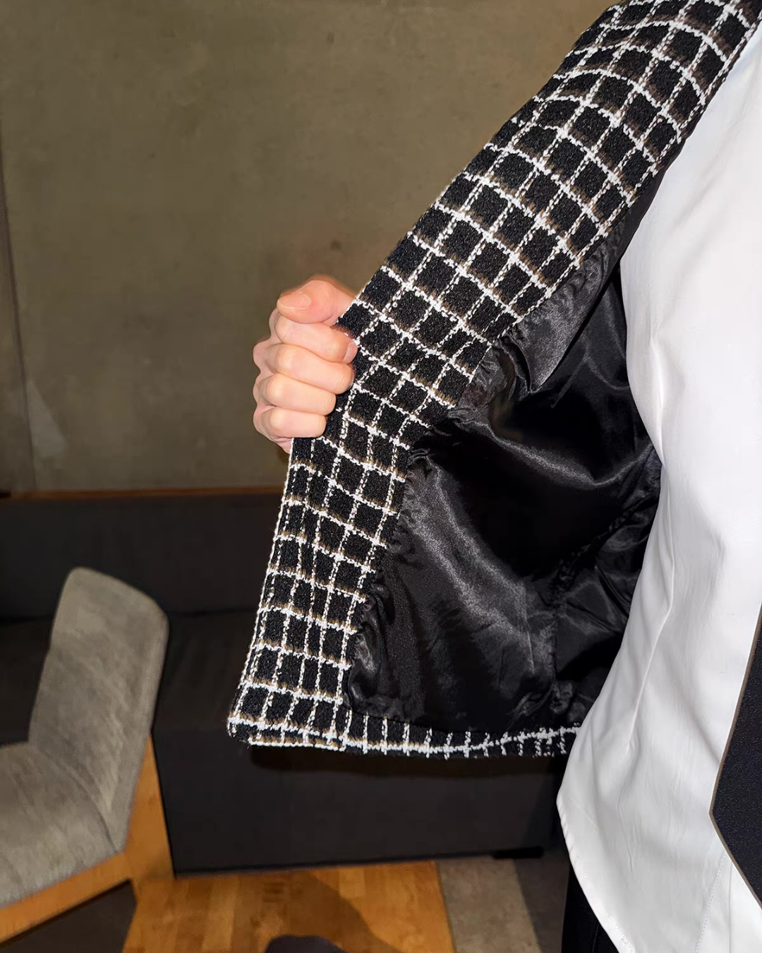 メンズのジャケットの前を開けた内側の接写。黒いサテン調の裏地と、黒白格子ツイードの前立て、白シャツが見える