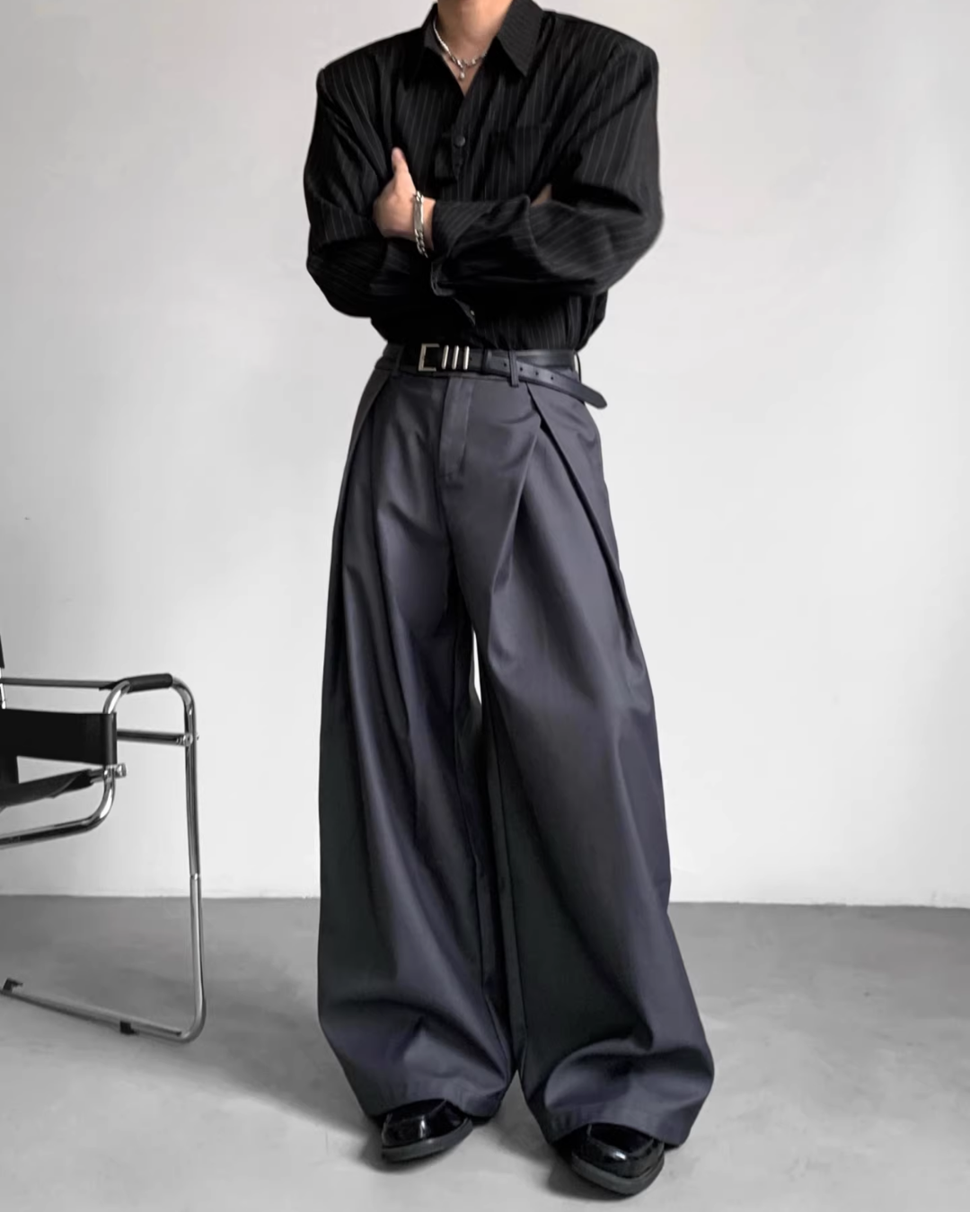 メンズの黒のピンストライプシャツとグレー系ワイドスラックス。スラックスはウエストにベルト装着、脇にタックが入り、ドレープ感を持つシルエット。