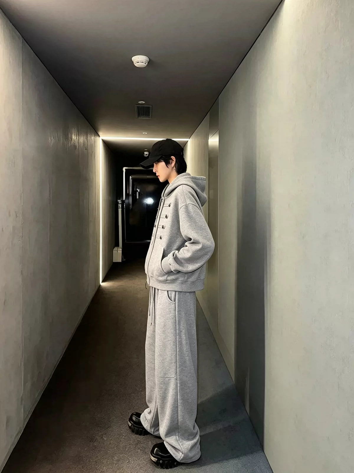 メンズのグレーのセットアップを真横から写した全身。パーカーの胸のボタン飾りと、裾がたまるワイドパンツの形が分かる。