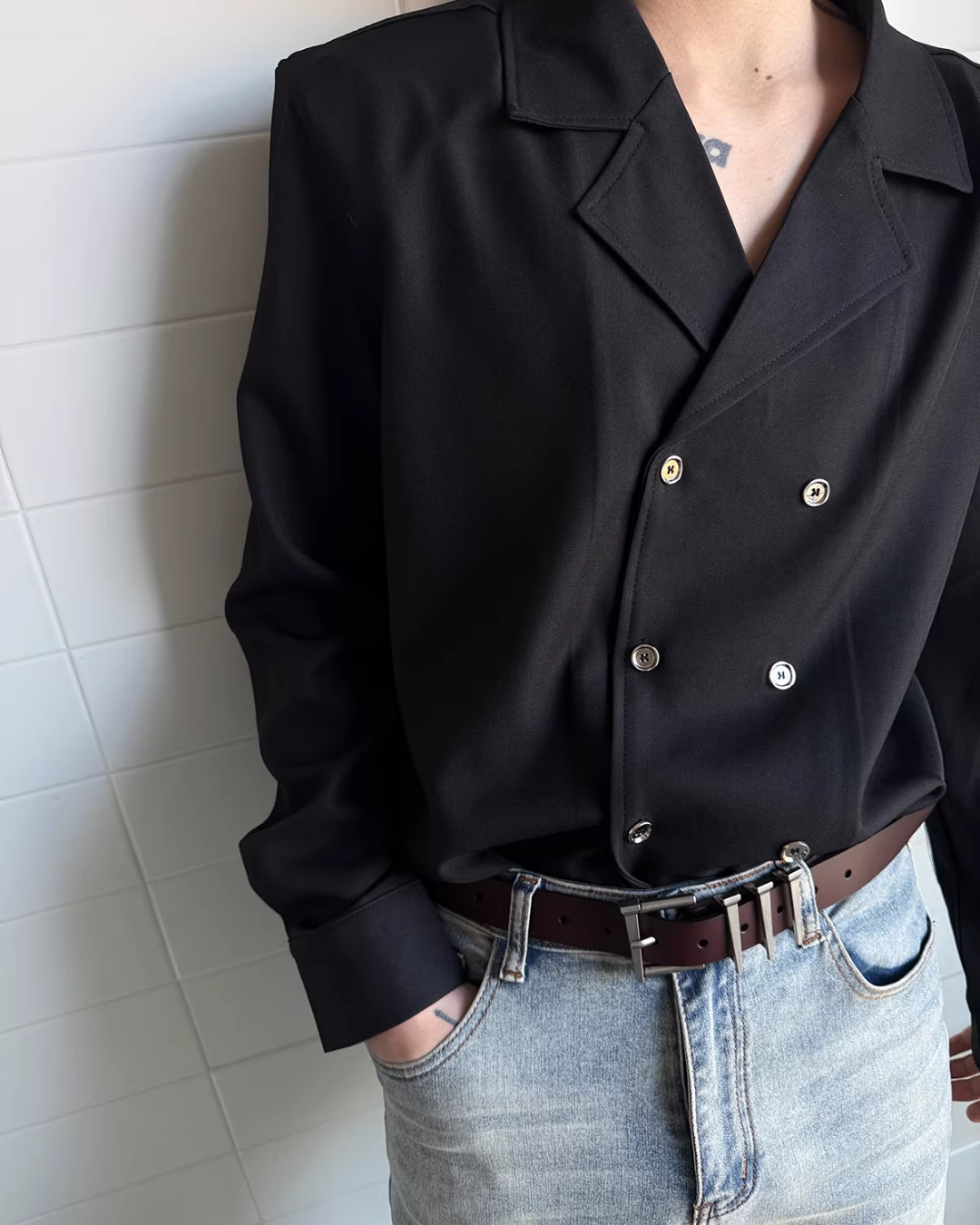 メンズの黒のダブルブレストシャツの胸元から腰まで。銀と金色が混じる光のボタン6個と、ステッチのある切替襟。