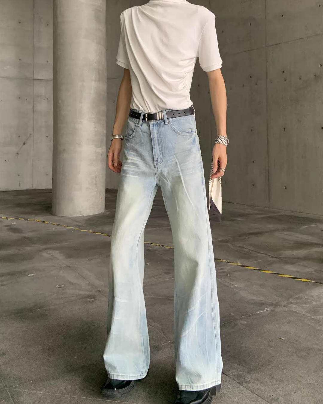メンズの淡いブルーのフレアデニムパンツ。白カットソーと黒ベルトを合わせ、腿のヒゲ加工と膝下から広がる裾を正面から見せた着用。